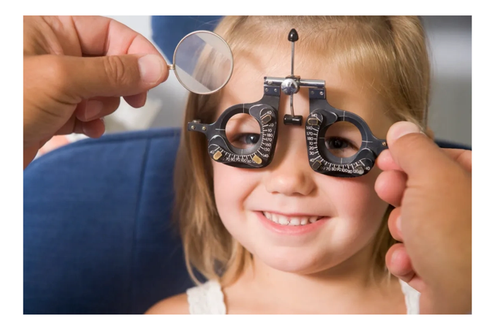 A young girl smiling during an eye exam with a phoropter.