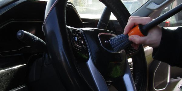 Hand cleaning a car steering wheel with a brush.