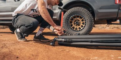 Man inflating an air mattress beside a truck on a dirt road.