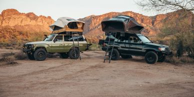 Two SUVs with rooftop tents set up in a desert landscape at sunset.