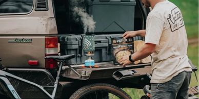 Man cooking pasta on a portable stove at the back of a Land Cruiser.