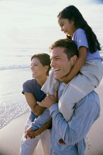 A father carrying his laughing daughter on his shoulders at the beach.