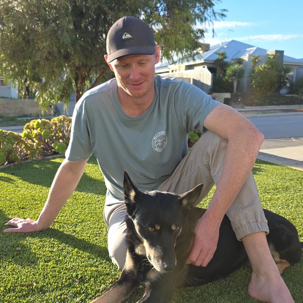 Man sitting on grass with a black dog on a sunny day.