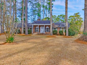 Brick house with white columns surrounded by tall pine trees.