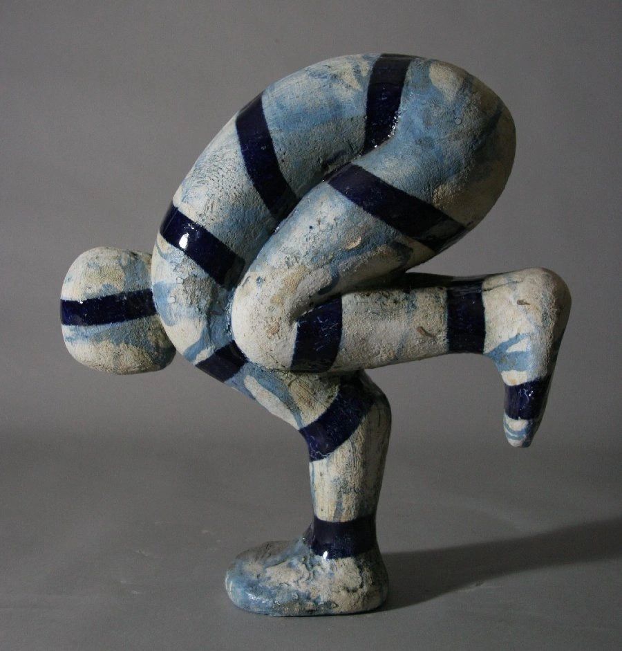 A small figurative ceramic sculpture depicting a figure in the yoga crow pose. 