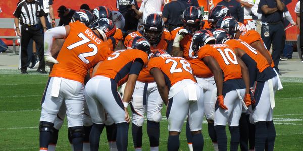 Denver Broncos players huddle on the football field during a game.