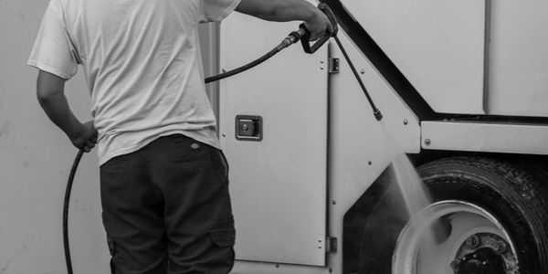 Person pressure washing a vehicle's tire in black and white.