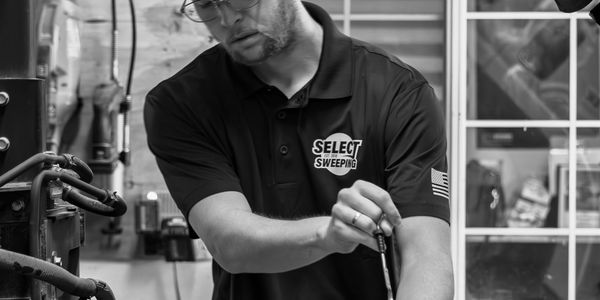 Man in a Select Sweeping shirt working with a tool in a workshop.
