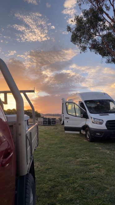 White van with open door on grassy field during sunset.