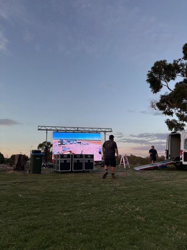 Outdoor event setup with a large screen at dusk.