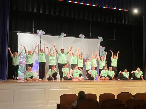 Group of performers in green shirts celebrating on stage with balloons.