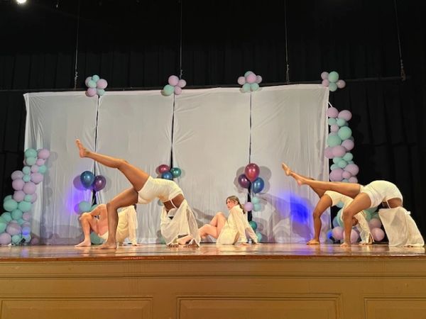 Dancers performing a graceful routine on stage with balloons and pastel decorations.