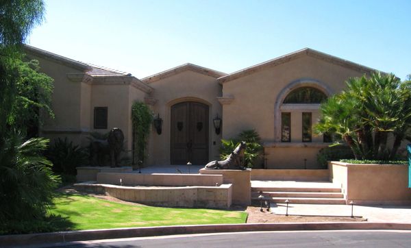 Modern house with lion statues and lush greenery.