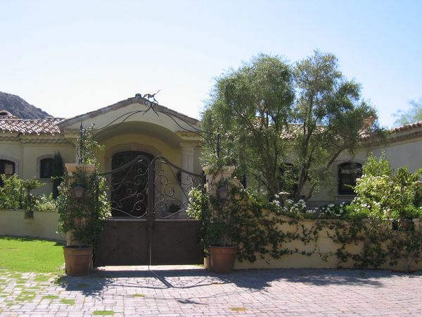 Elegant house entrance with ornate wrought iron gate and lush greenery.