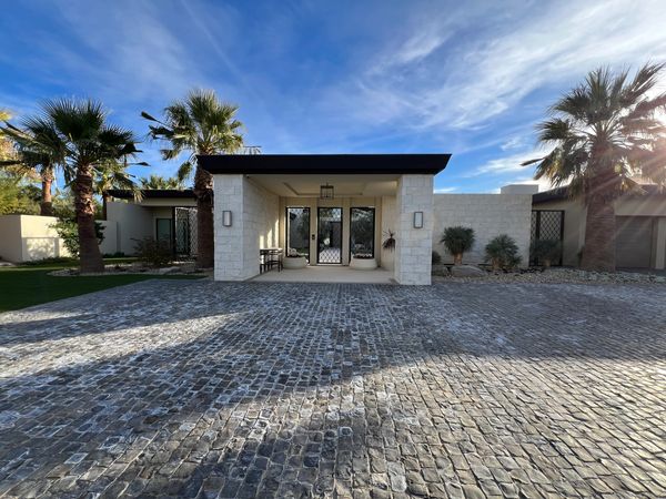 Modern house entrance with stone facade and palm trees under a blue sky.