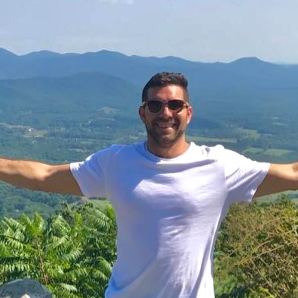 Man in white shirt spreading arms with mountain view.