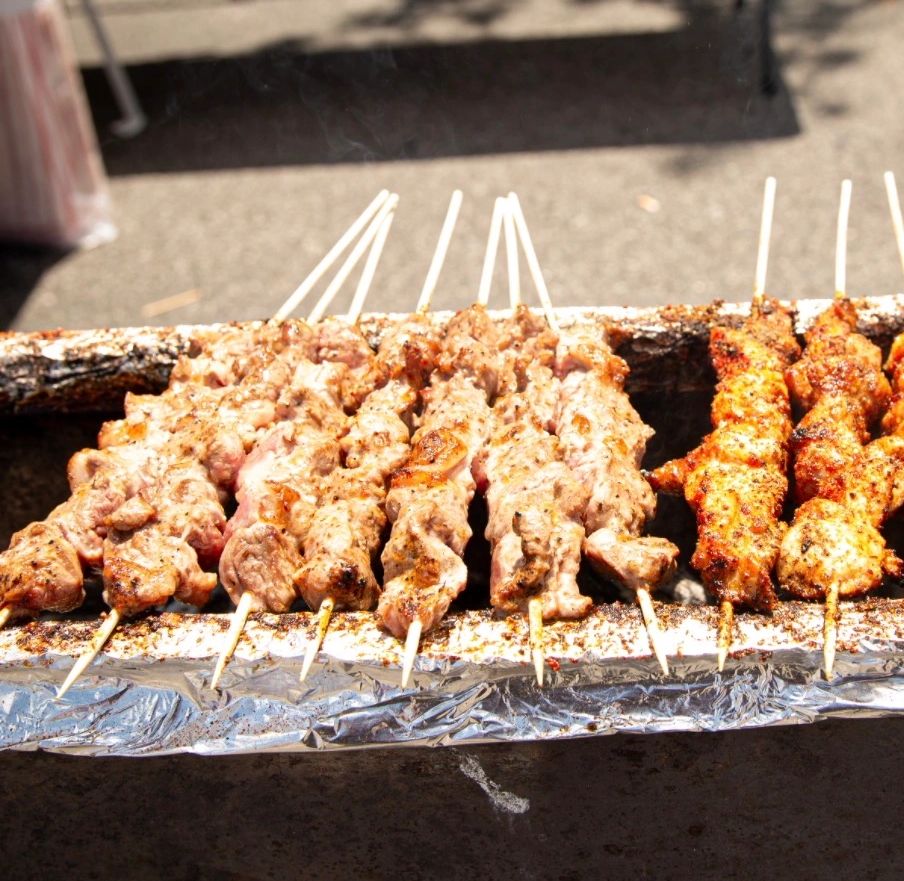 Grilled meat skewers cooking over hot coals outdoors.