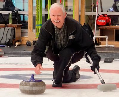 Man playing curling, releasing stone on ice.