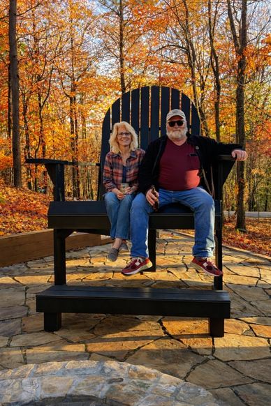 A couple sitting on a giant black wooden chair in an autumn forest.