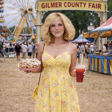 Woman in yellow dress holding funnel cake and drink at Gilmer County Fair.