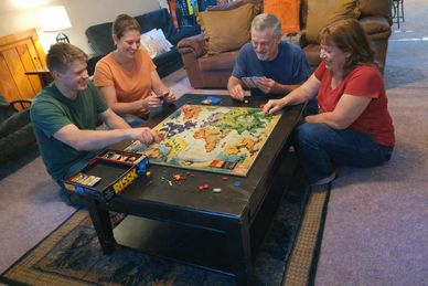 Four adults enjoy playing a strategic board game around a coffee table.