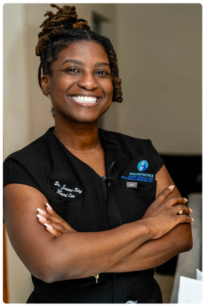 Smiling healthcare professional in black scrubs with arms crossed.
