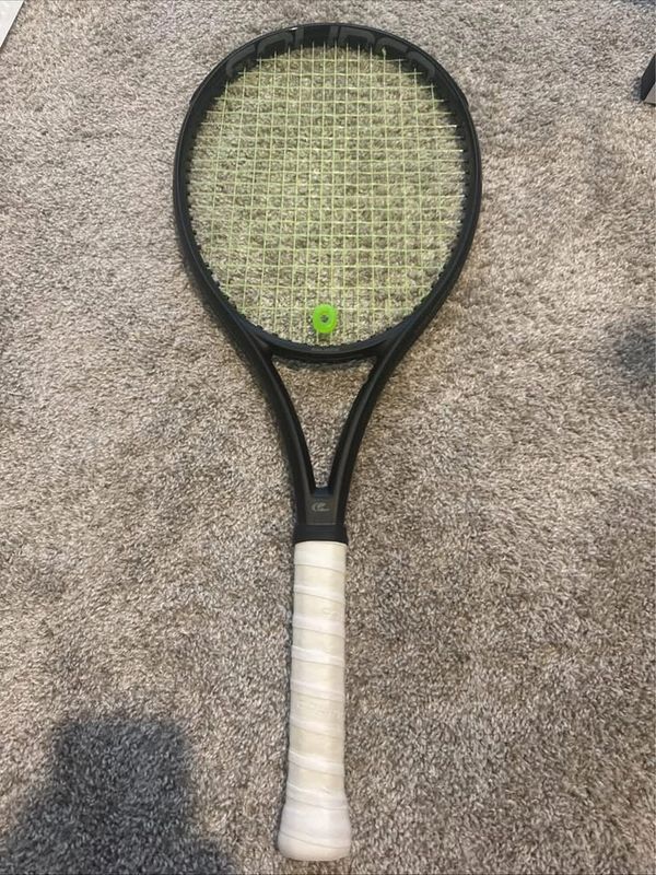 Black tennis racket with white grip on carpet.
