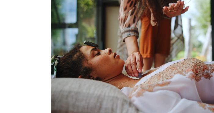 A person receiving a reiki healing crystal treatment, lying down with a stone on their forehead.