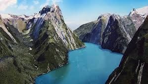 Steep green mountains surrounding a bright blue fjord under a partly cloudy sky