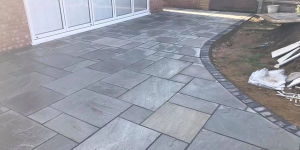 Newly installed grey stone patio with a curved edge and brick border.