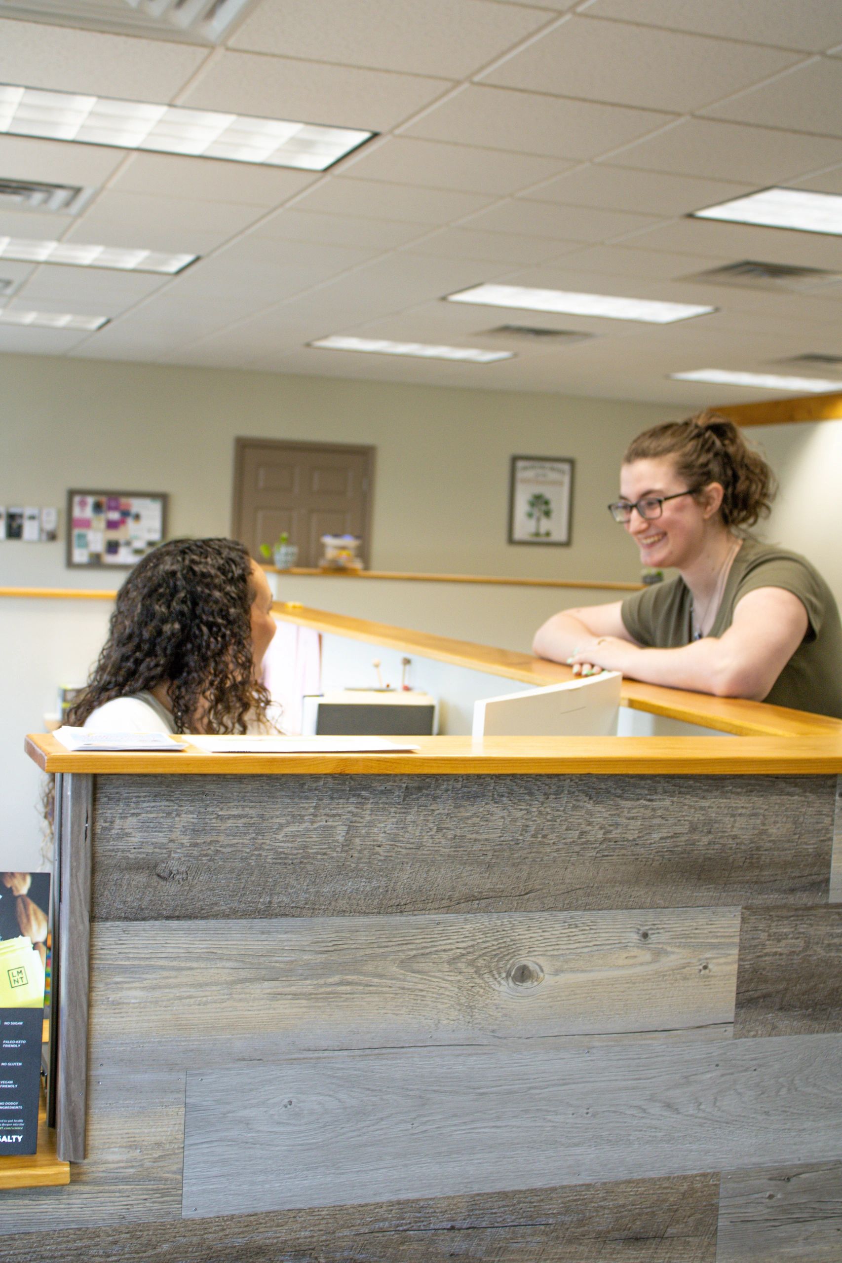 Two women chatting over a reception desk in an office.