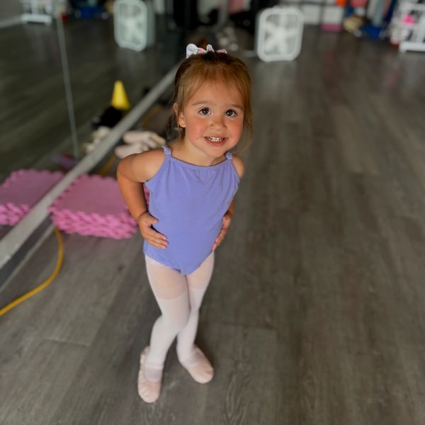Smiling toddler in ballet outfit posing indoors.