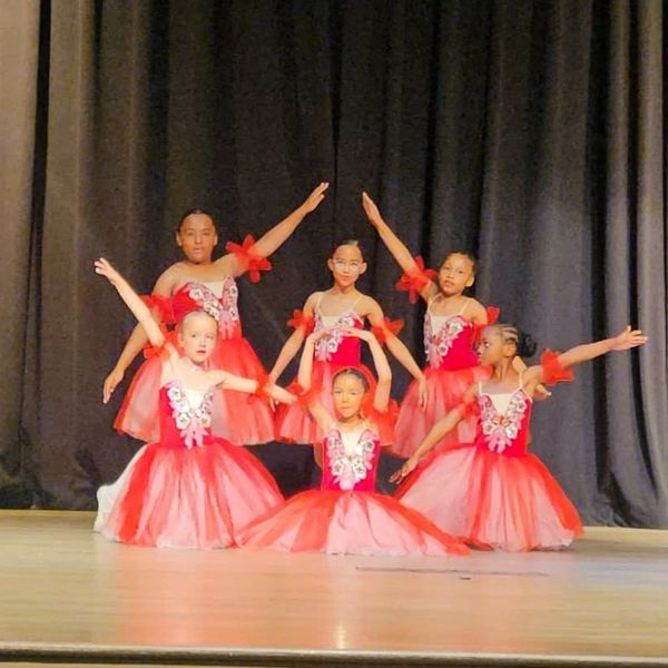 Young girls in red ballet costumes performing on stage.