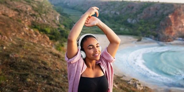 Woman enjoying music with headphones near a scenic coastline.