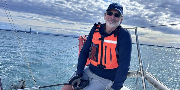 Smiling man in orange life vest on a sailboat.