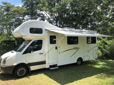 White camper van with an awning extended in a green park.
