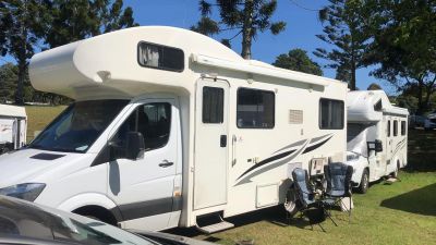 White RV parked on grass with trees in the background.