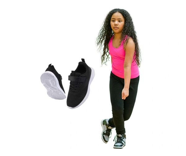 Girl wearing black shoes and pink top next to a pair of black sports shoes.