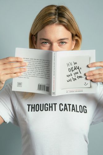 Person holding a book titled "It'll Be Okay, And You Will Be Too."