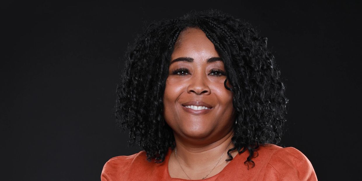 Woman in an orange dress smiling against a black background.