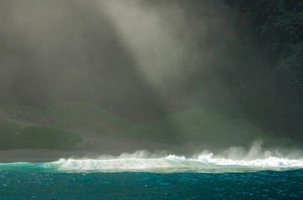 Sunlight breaks through mist above ocean waves near shore.
