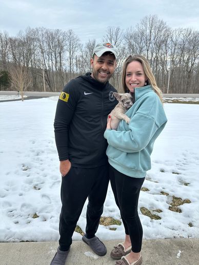 Couple smiling outdoors in winter holding a small dog.