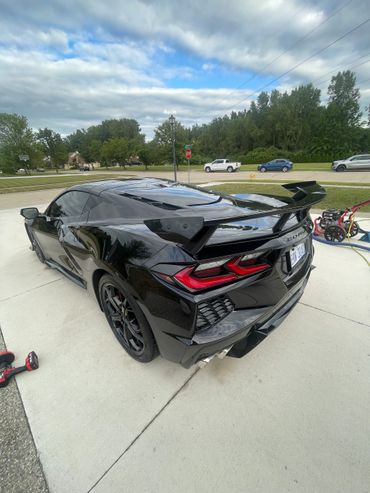 Sleek black sports car with a prominent rear spoiler parked on a driveway.