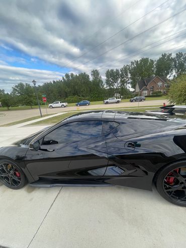 Sleek black sports car parked on a driveway under a cloudy sky.