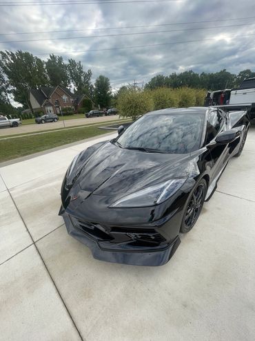 Shiny black sports car parked on a driveway under a cloudy sky.