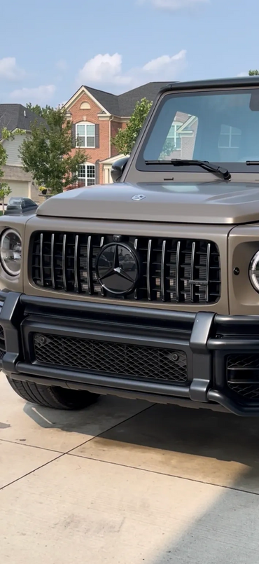 Front view of a matte brown Mercedes G-Class SUV parked on a driveway.