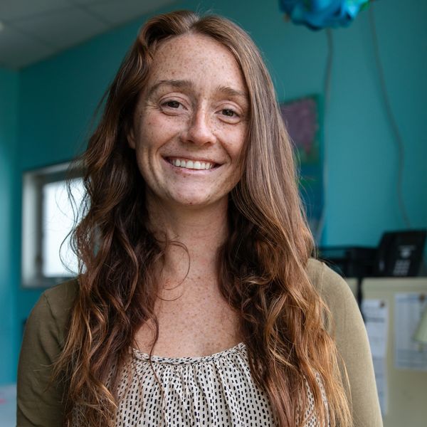 Smiling woman with long red hair and freckles in a cozy indoor setting.