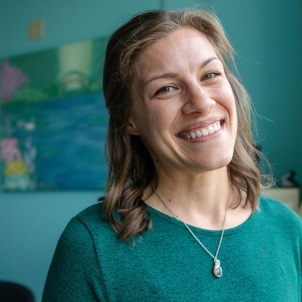 Smiling woman in green sweater with pendant necklace indoors.