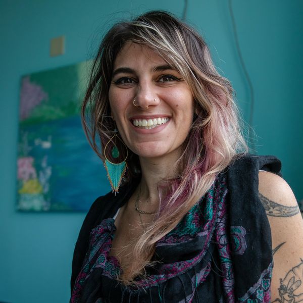 Smiling woman with colorful hair and tattoos in a cozy room.