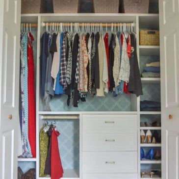 A custom reach-in closet with white cabinetry, open shelving, hanging clothes, and drawers